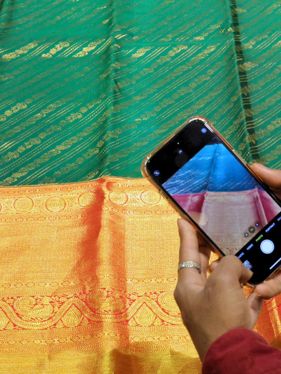 A close-up of handwoven silk sarees in vibrant colors like pink, green, and blue with intricate zari designs.